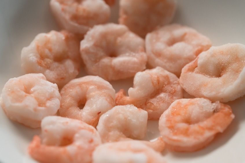 Un plato blanco cubierto con camarones cocidos sobre una mesa.