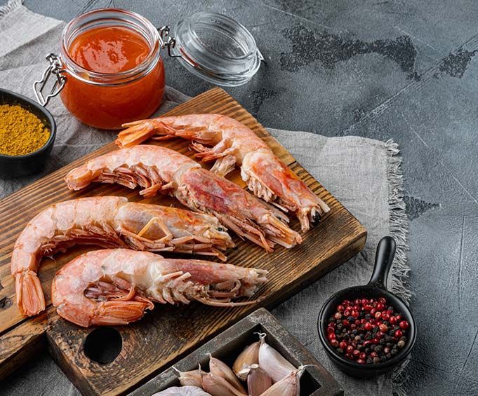 Los camarones están sentados en una tabla de cortar de madera al lado de un frasco de salsa.