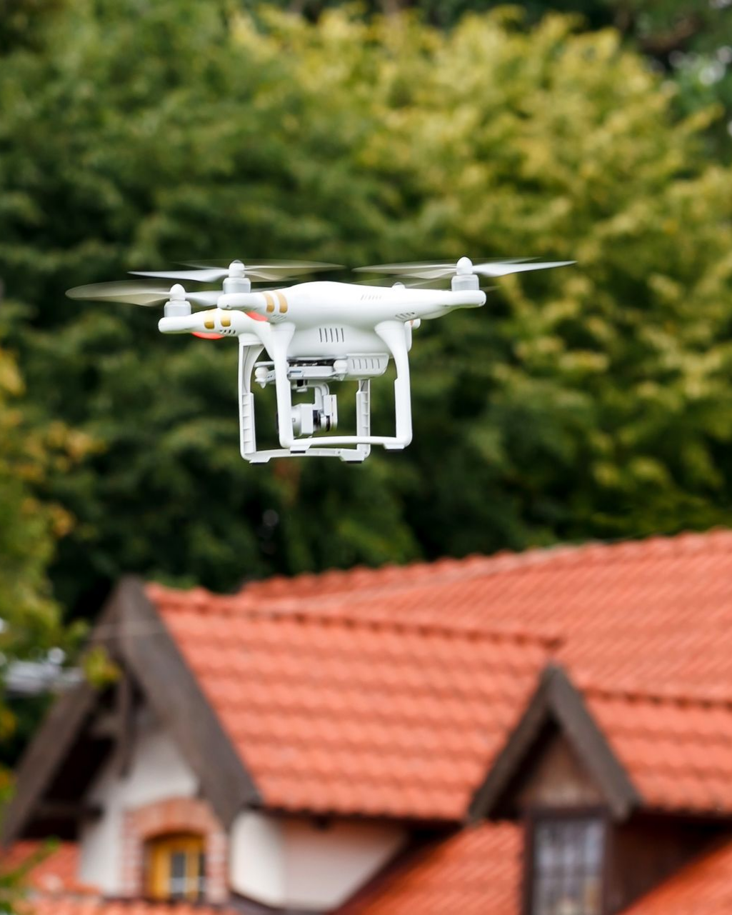 Un drone blanc survole un toit de tuiles.