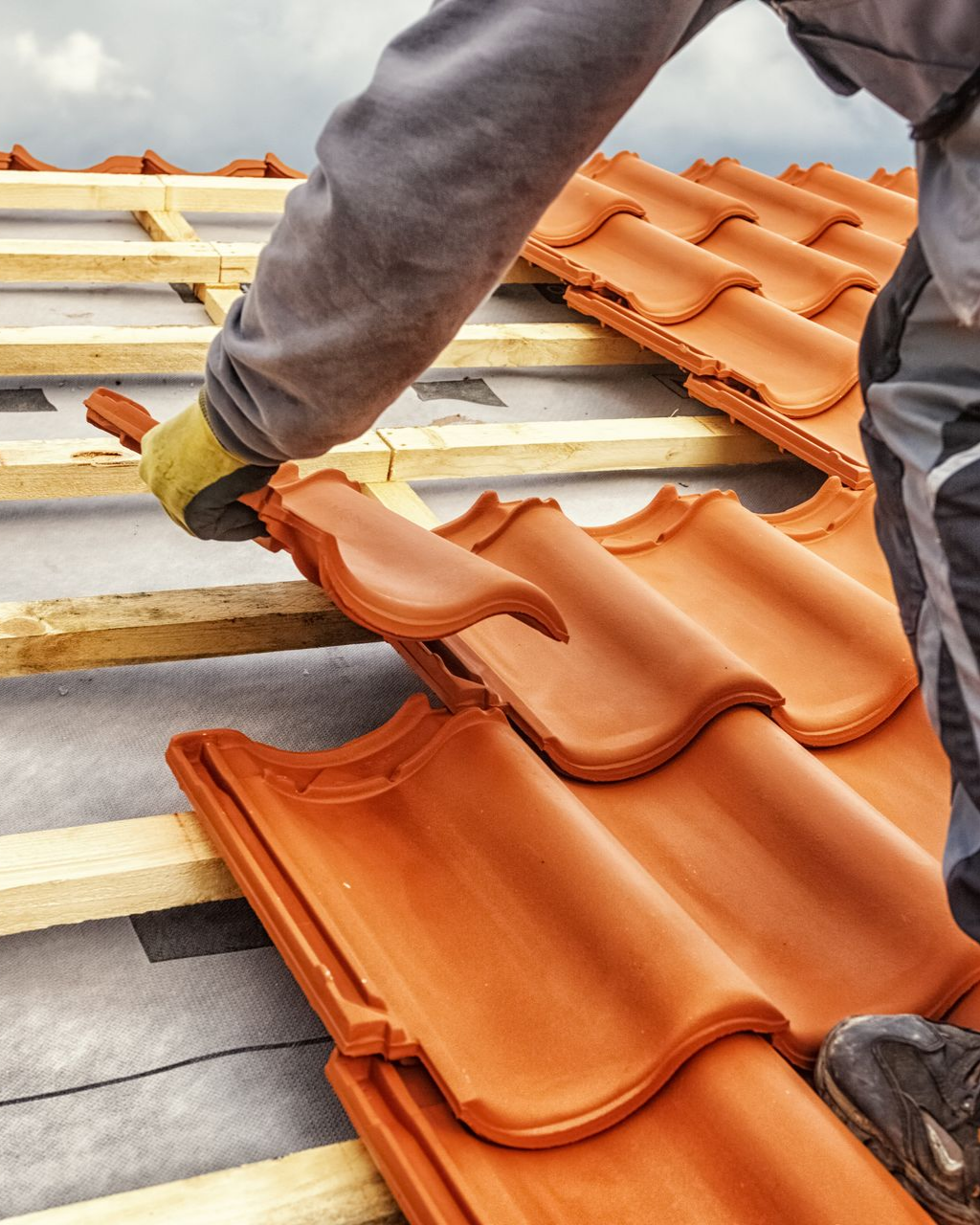 Un couvreur pose des tuiles en terre cuite sur un toit.
