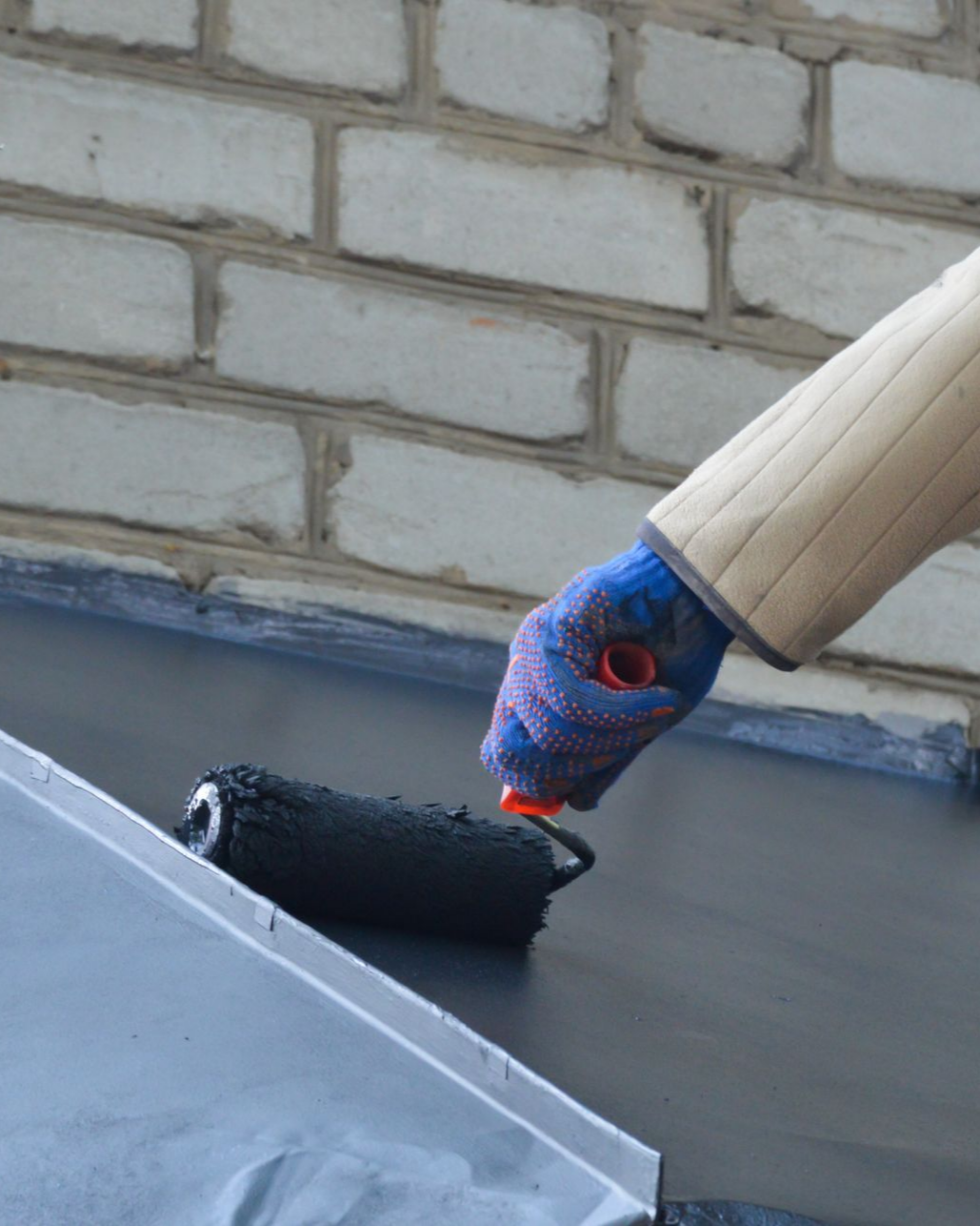 Une personne gantée utilise un rouleau pour appliquer une peinture noire sur un toit.