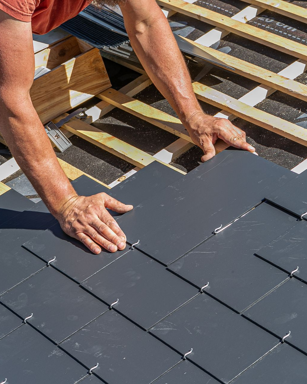 Un couvreur pose des ardoises sur un toit.