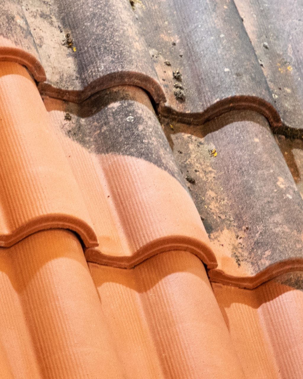 Tuiles de toit en terre cuite rouge, nettoyées à moitié, montrant un contraste entre les parties propres et sales.