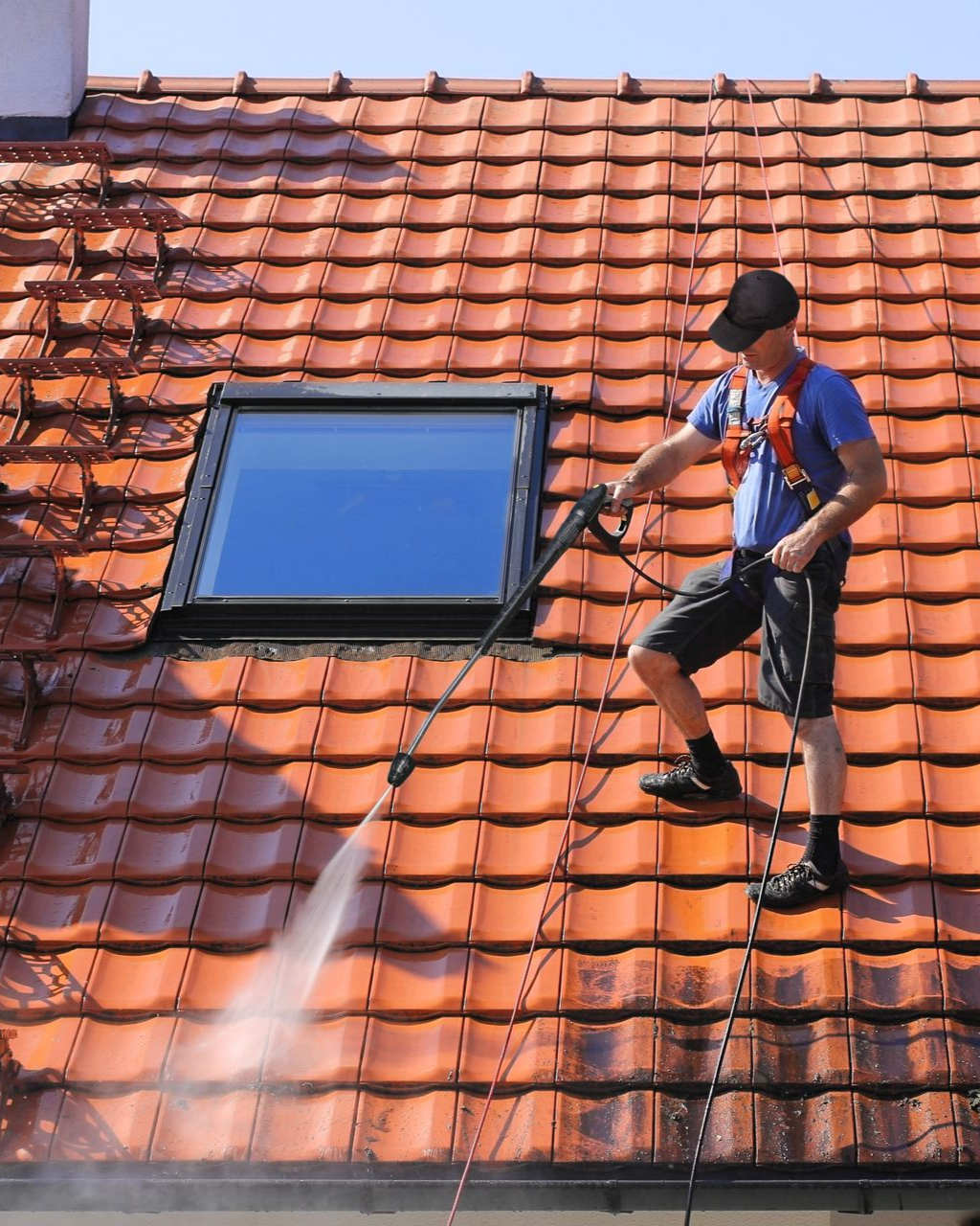 Un couvreur qui nettoie une toiture à l'aide d'un nettoyeur à haute pression.