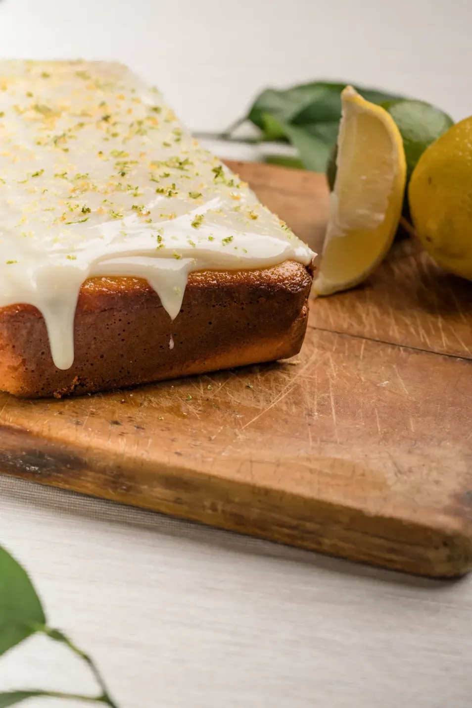 Un trozo de pastel de limón con glaseado blanco reposa sobre una tabla de cortar de madera.