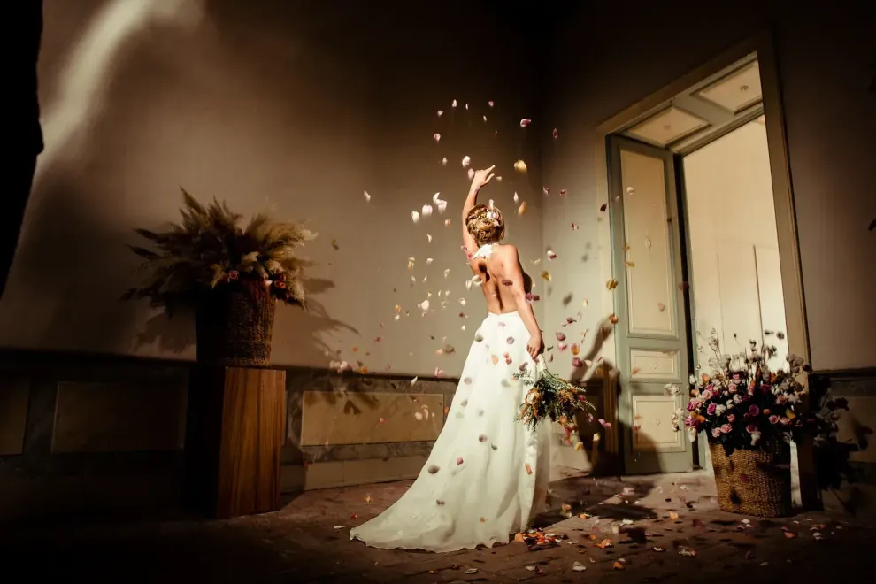 Una novia con un vestido de novia está lanzando pétalos al aire.
