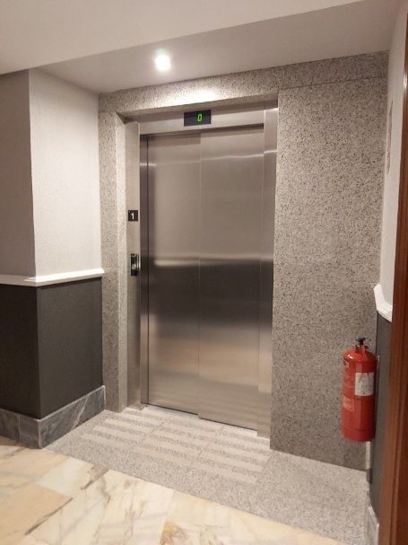 Un ascensor de acero inoxidable está en un pasillo al lado de un extintor de incendios.