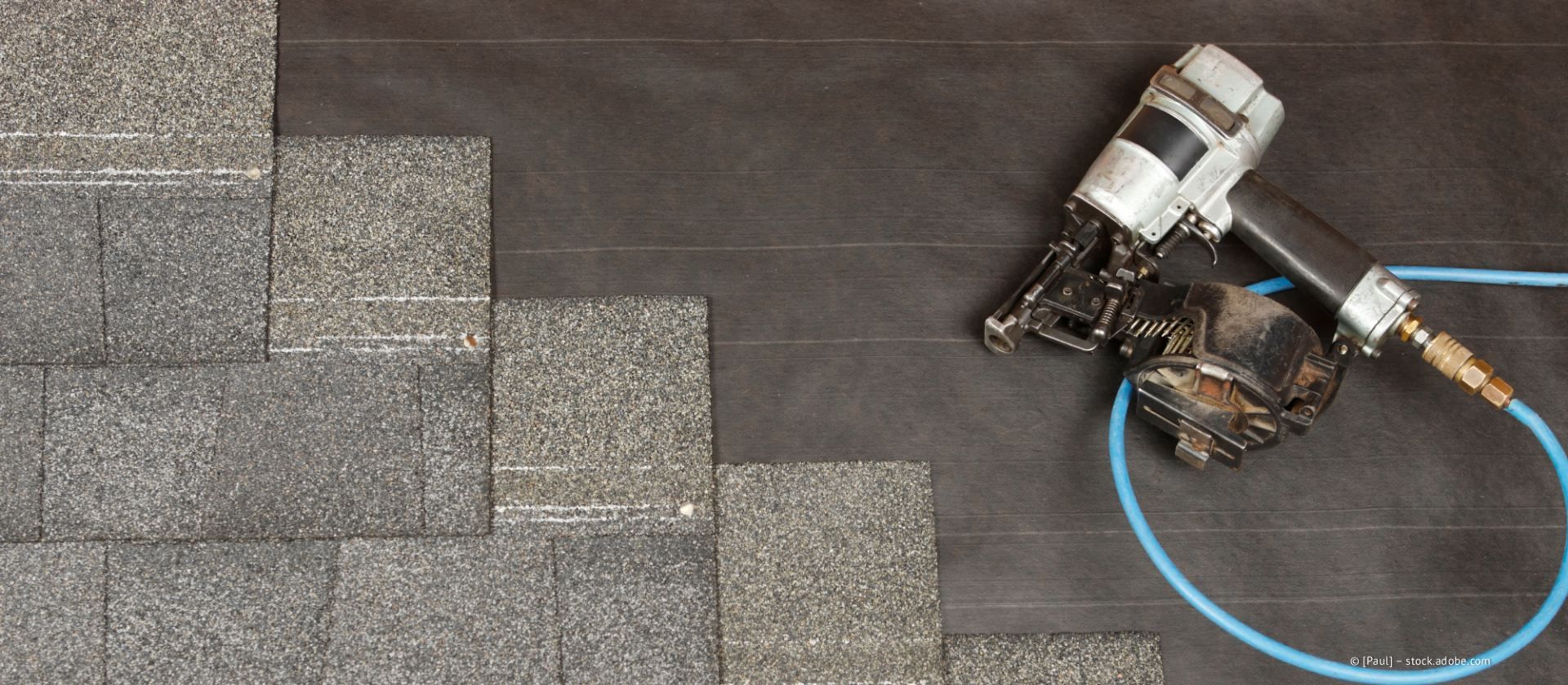 Ein Dachdecker verlegt mit einem Nagler Asphaltschindeln.