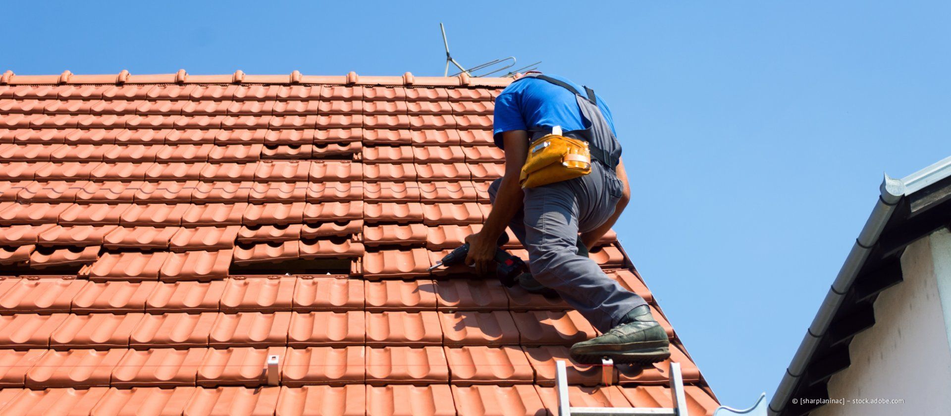 Eine Person repariert an einem sonnigen Tag Dachziegel aus Ton.