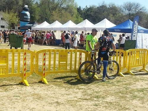 Un hombre está de pie junto a una bicicleta en un campo rodeado de barreras amarillas.