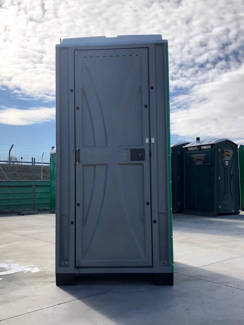 Un baño portátil gris y verde está en un estacionamiento.