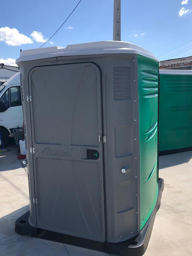 Un baño portátil verde y gris está en un estacionamiento.