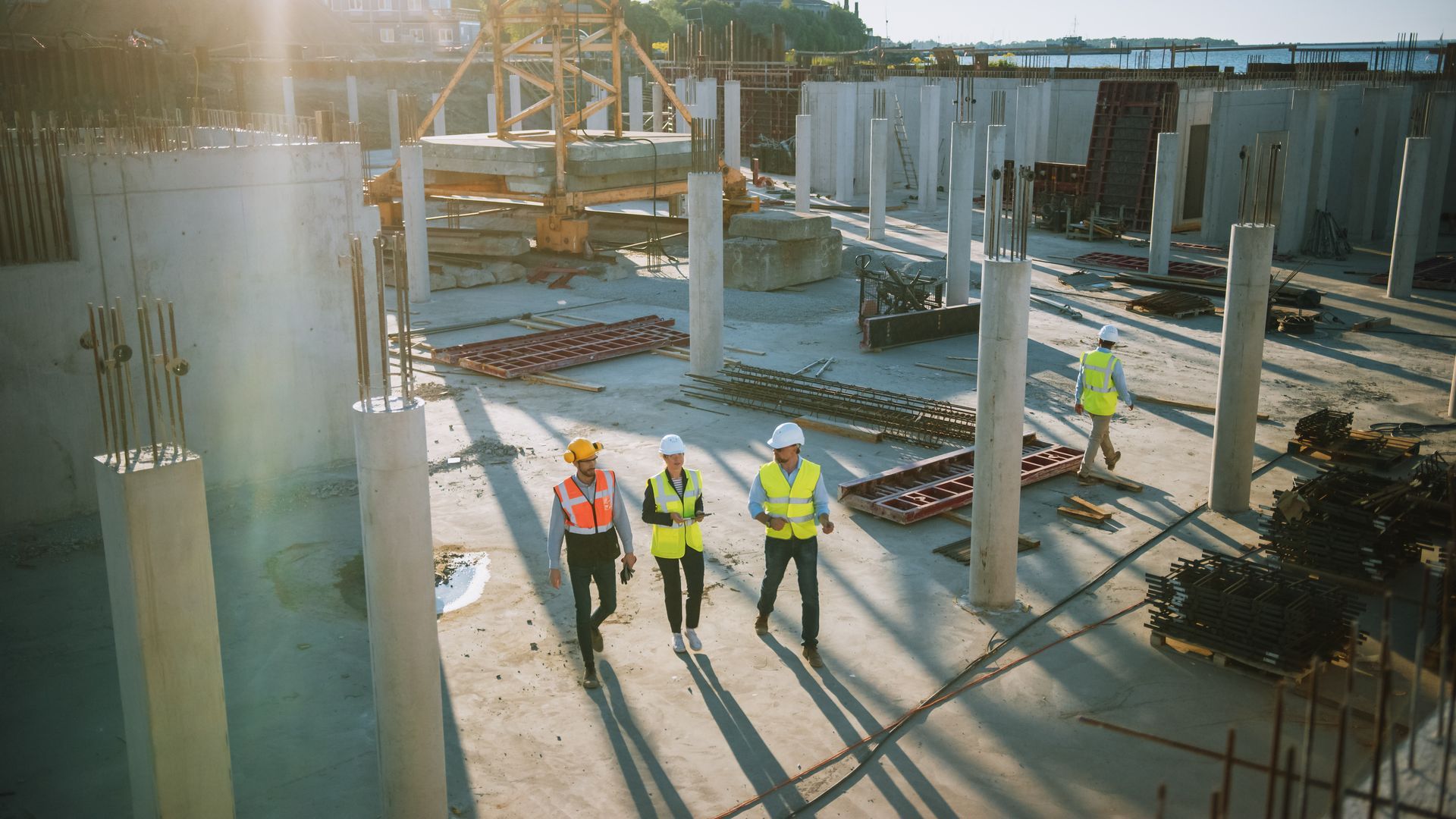 Baustelle mit Bauplänen, Schutzhelm und Stadtkulisse mit Kränen im Hintergrund.