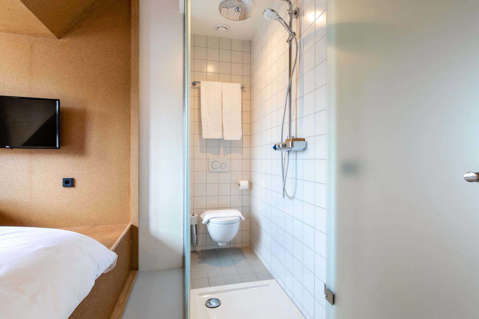 A bathroom with a toilet , shower , and television.