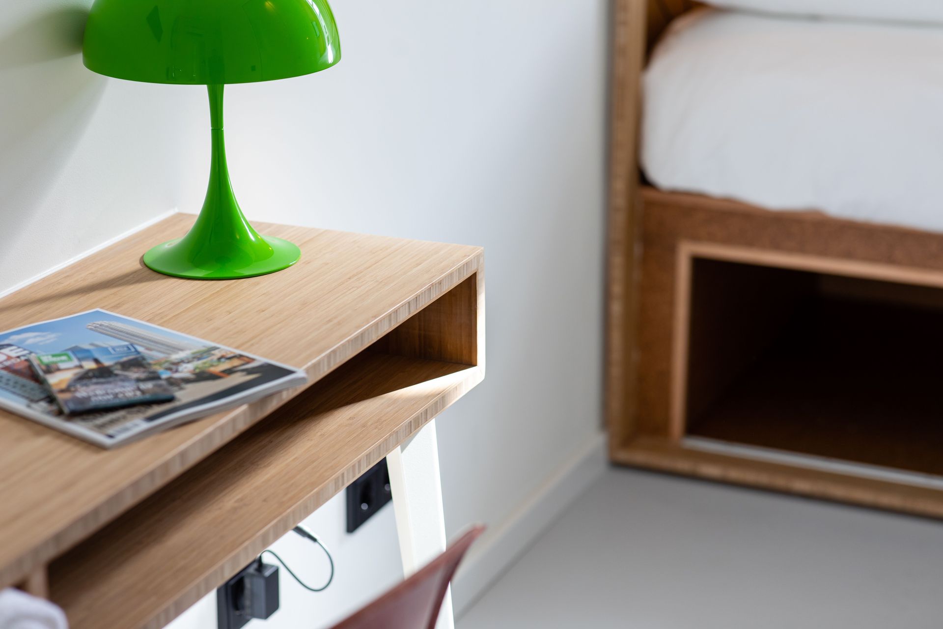 A green lamp is sitting on a wooden table next to a bed.