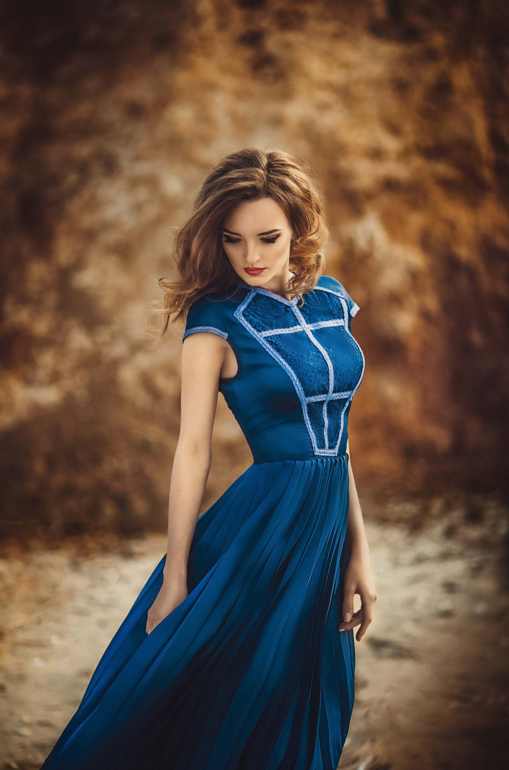 Una mujer con un vestido largo azul está parada en la arena.