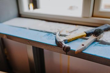 Un martillo de orejas y un pequeño cepillo multiusos descansan sobre una superficie de construcción cubierta de pintura azul