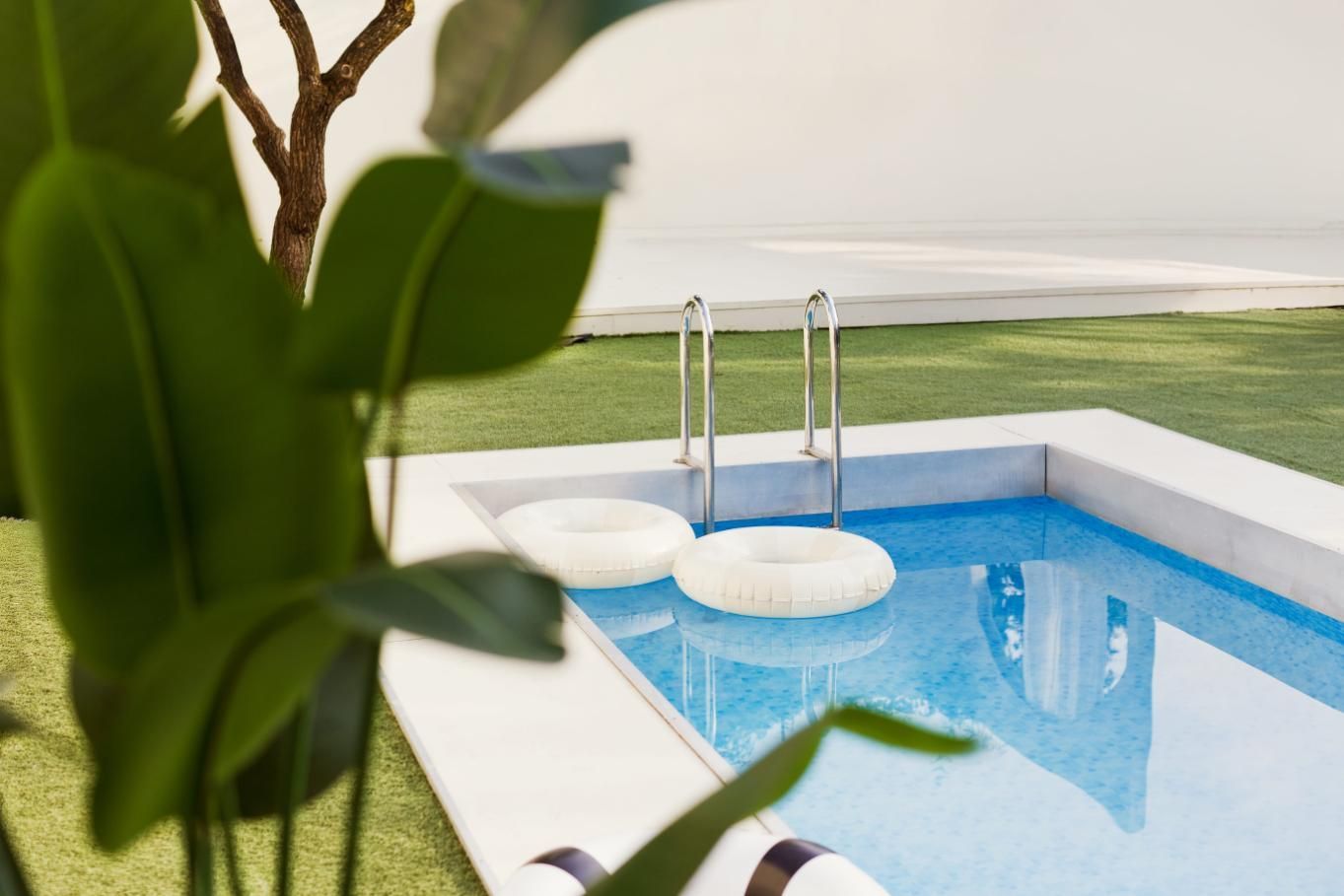 Una pequeña piscina rectangular de color azul brillante con una escalera plateada y dos flotadores blancos en el agua.