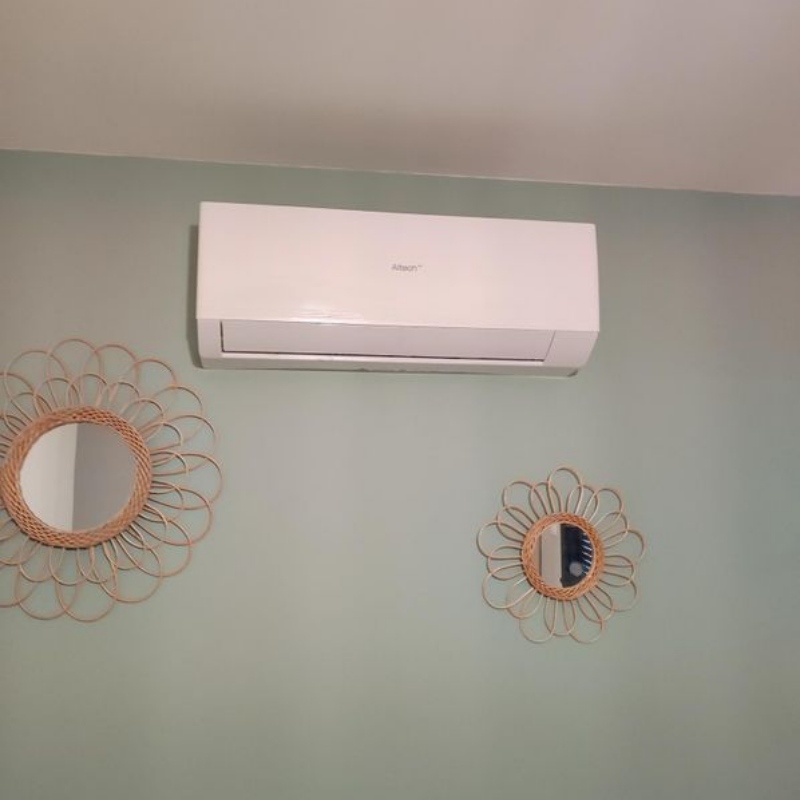 Climatiseur blanc mural au-dessus de deux miroirs soleil dorés sur un mur vert pâle