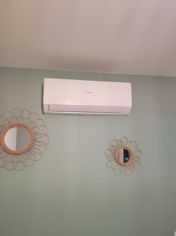 Climatiseur mural blanc au-dessus d'un mur vert pâle orné de deux miroirs décoratifs.