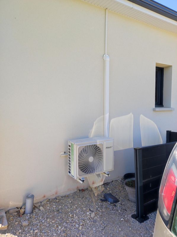 Unité de climatisation murale extérieure à côté d'une maison et d'une voiture garée sur une allée de gravier