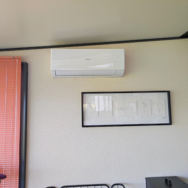 Climatiseur mural au-dessus d'une estampe abstraite encadrée sur un mur clair.