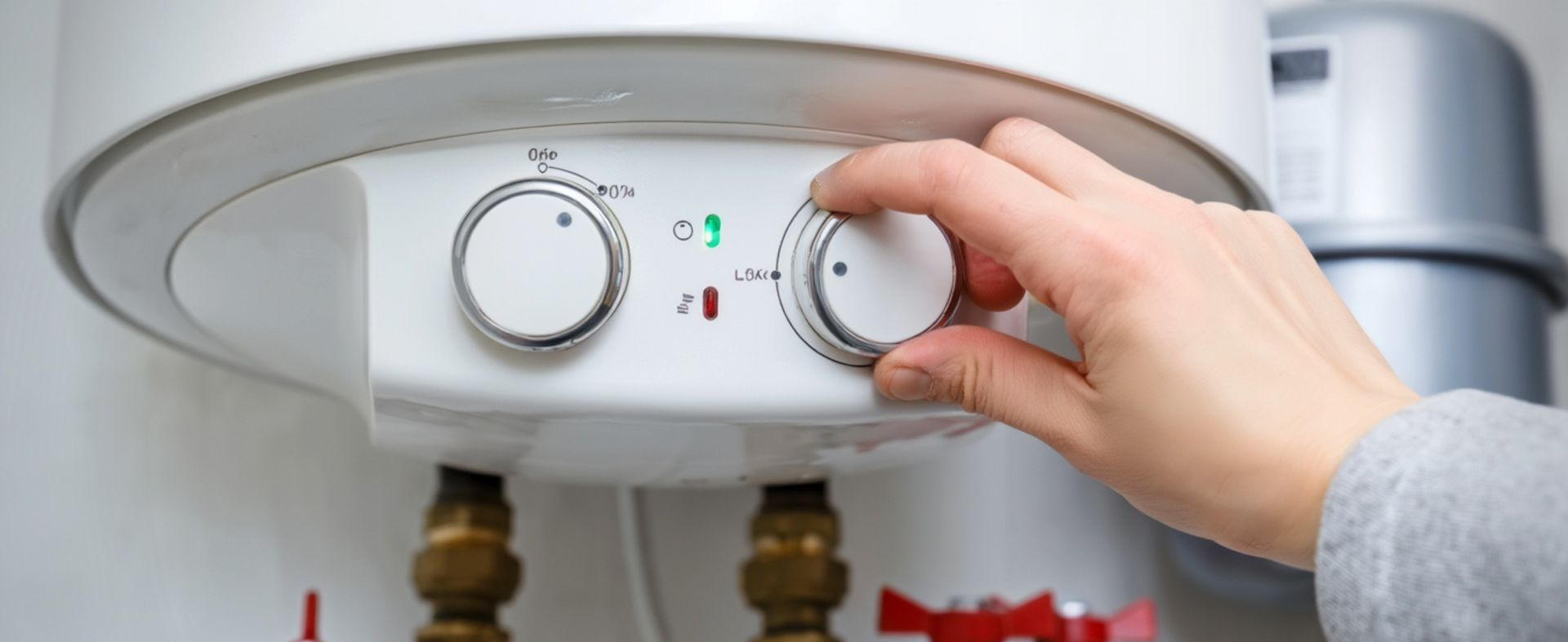 Une main tourne le bouton de commande blanc d'un chauffe-eau situé sous l'appareil, les indicateurs d'eau chaude et d'eau froide étant visibles.