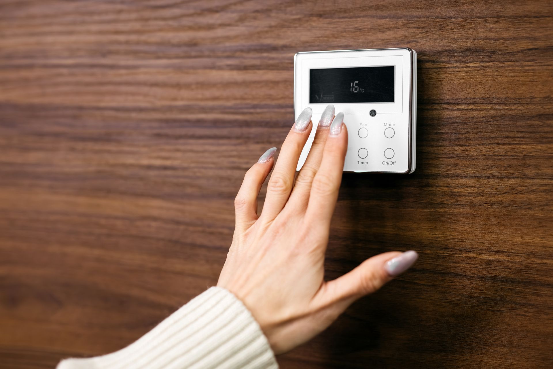 Réglage manuel d'un thermostat mural blanc sur un mur en bois.