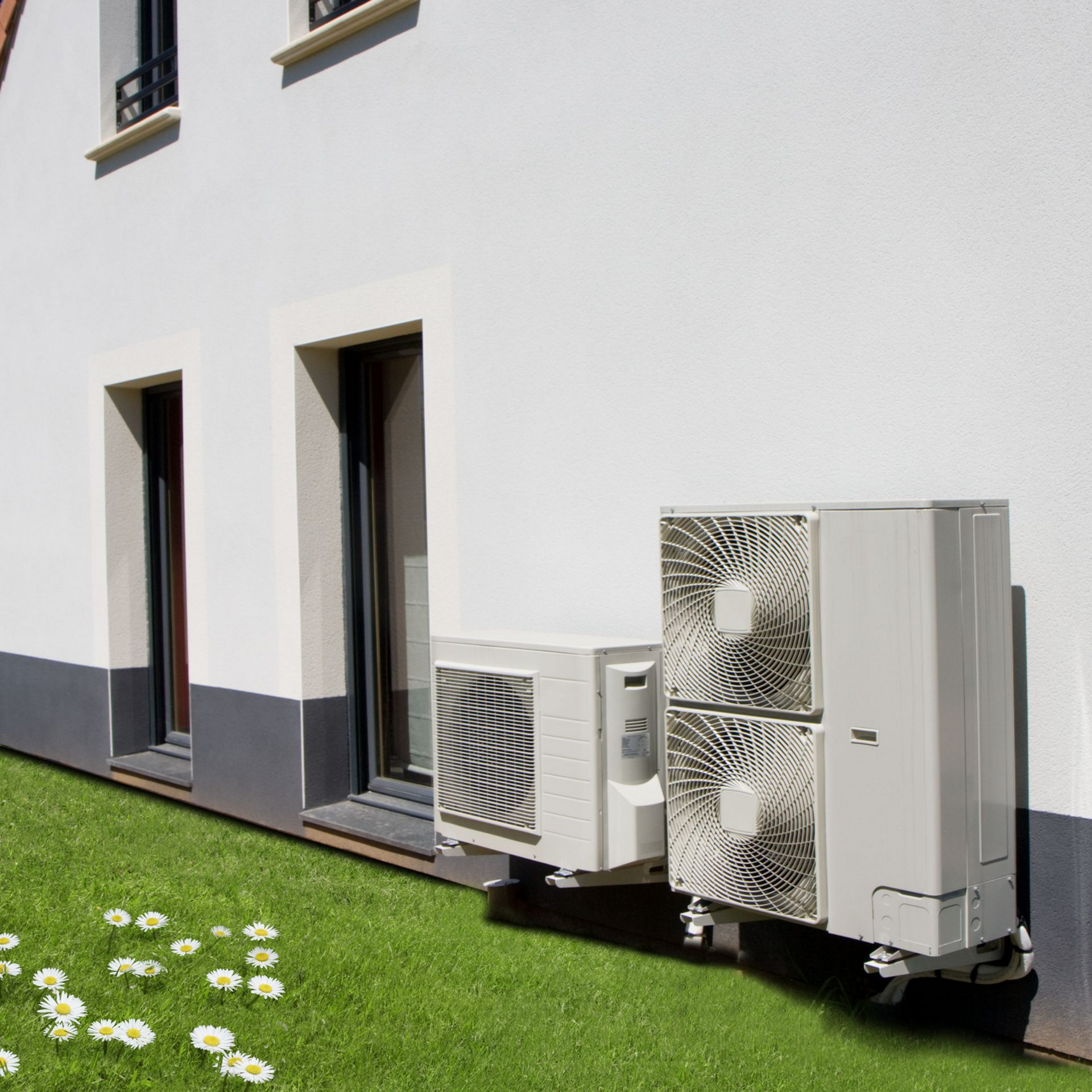 Mur extérieur d'un bâtiment moderne avec deux unités de climatisation, à côté d'une pelouse verte et de fleurs blanches.