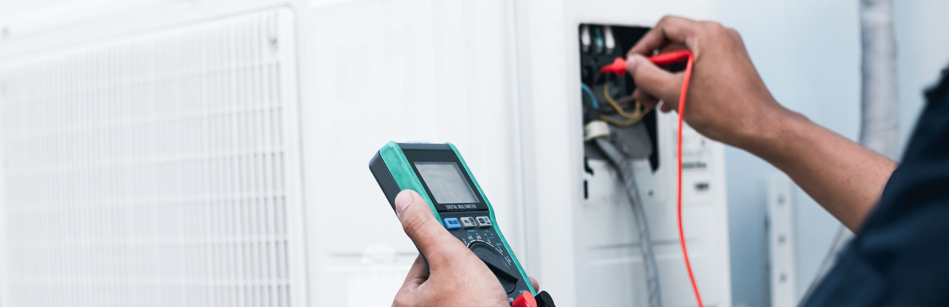 Un technicien teste un groupe de climatisation extérieur à l'aide d'un multimètre et d'une sonde.