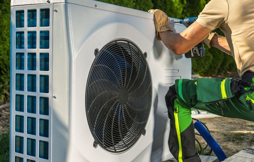 Un technicien répare un climatiseur extérieur équipé d'un grand ventilateur et de grilles d'aération latérales bleues.