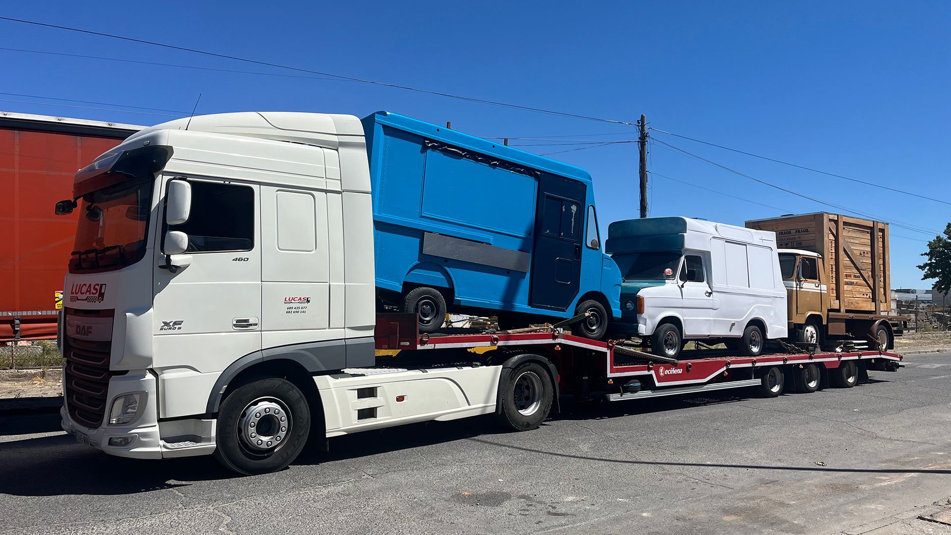 Un camión blanco transporta una camioneta azul y una camioneta blanca en un remolque.