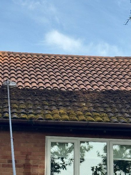Red-tiled roof with moss above a brick house and window against a blue sky