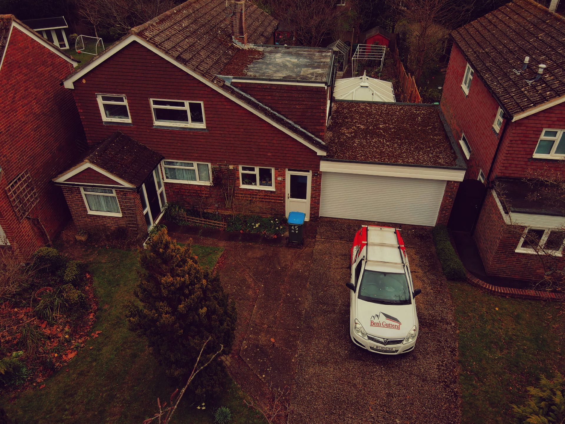 Aerial view of a red brick house with a white garage and a white car in the driveway.