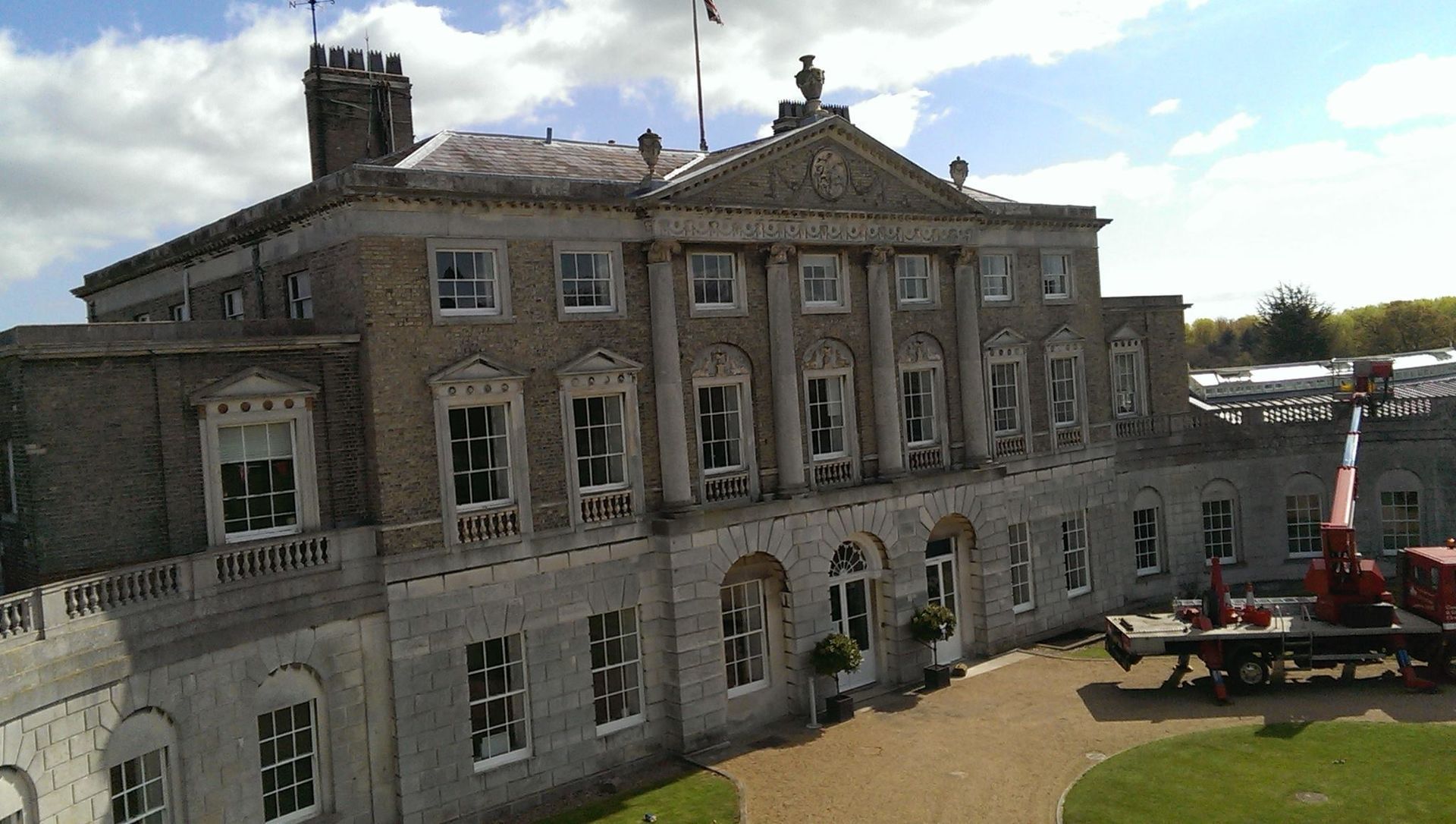 Historic stone mansion with ornate windows and construction equipment in front under a partly cloudy sky