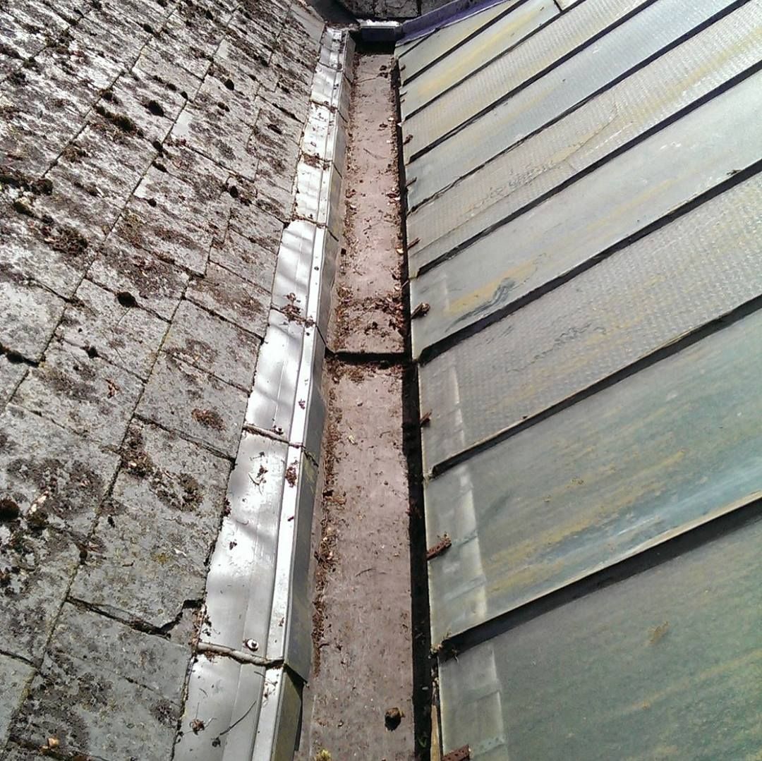 Close-up of a roof edge with cracked brick wall, metal flashing, and a narrow gutter seam with debris