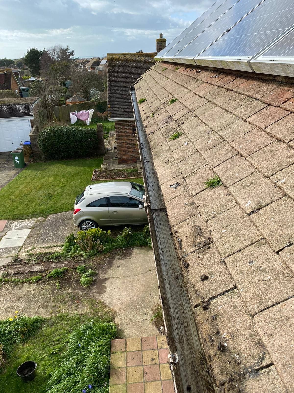 Rooftop view over a garden and parked silver car beside a house with solar panels.