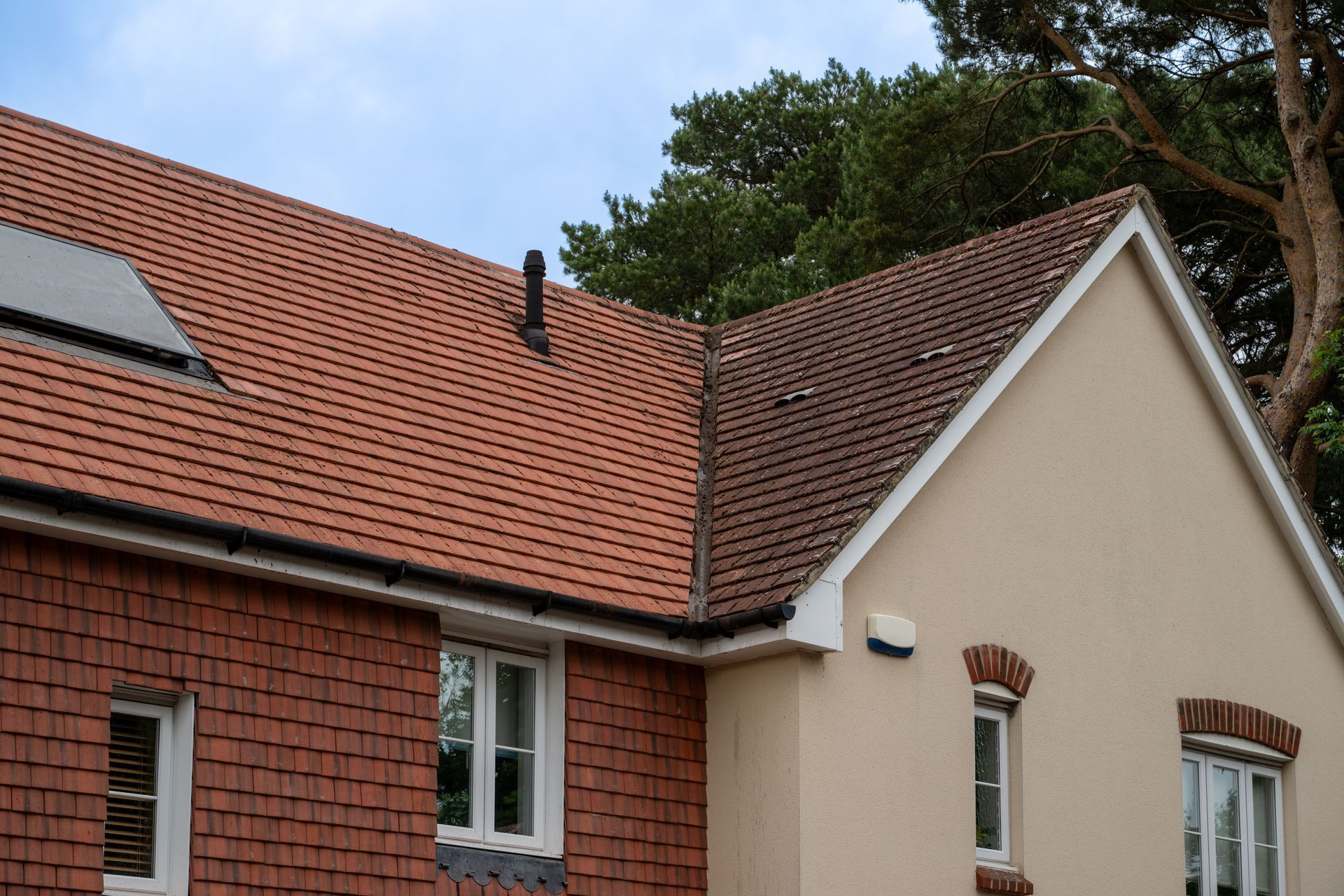 Red-tiled house roof with dormer windows and cream and brick exterior under trees