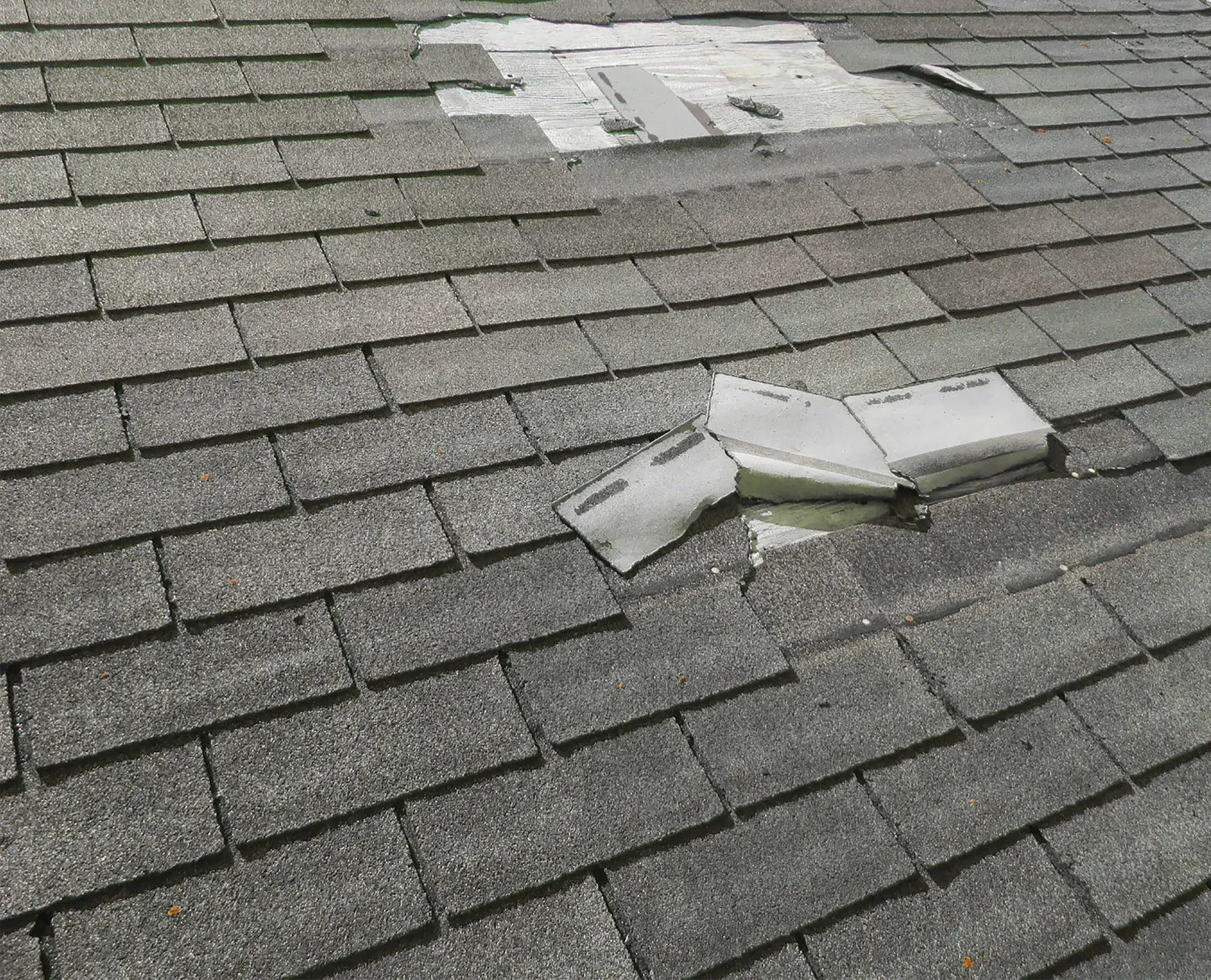 Shingled roof with a damaged section and scattered white debris on the shingles