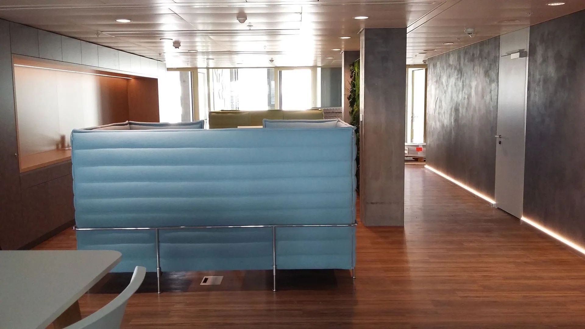 Espace d'accueil moderne avec comptoir en verre bleu, parquet et murs gris texturés.