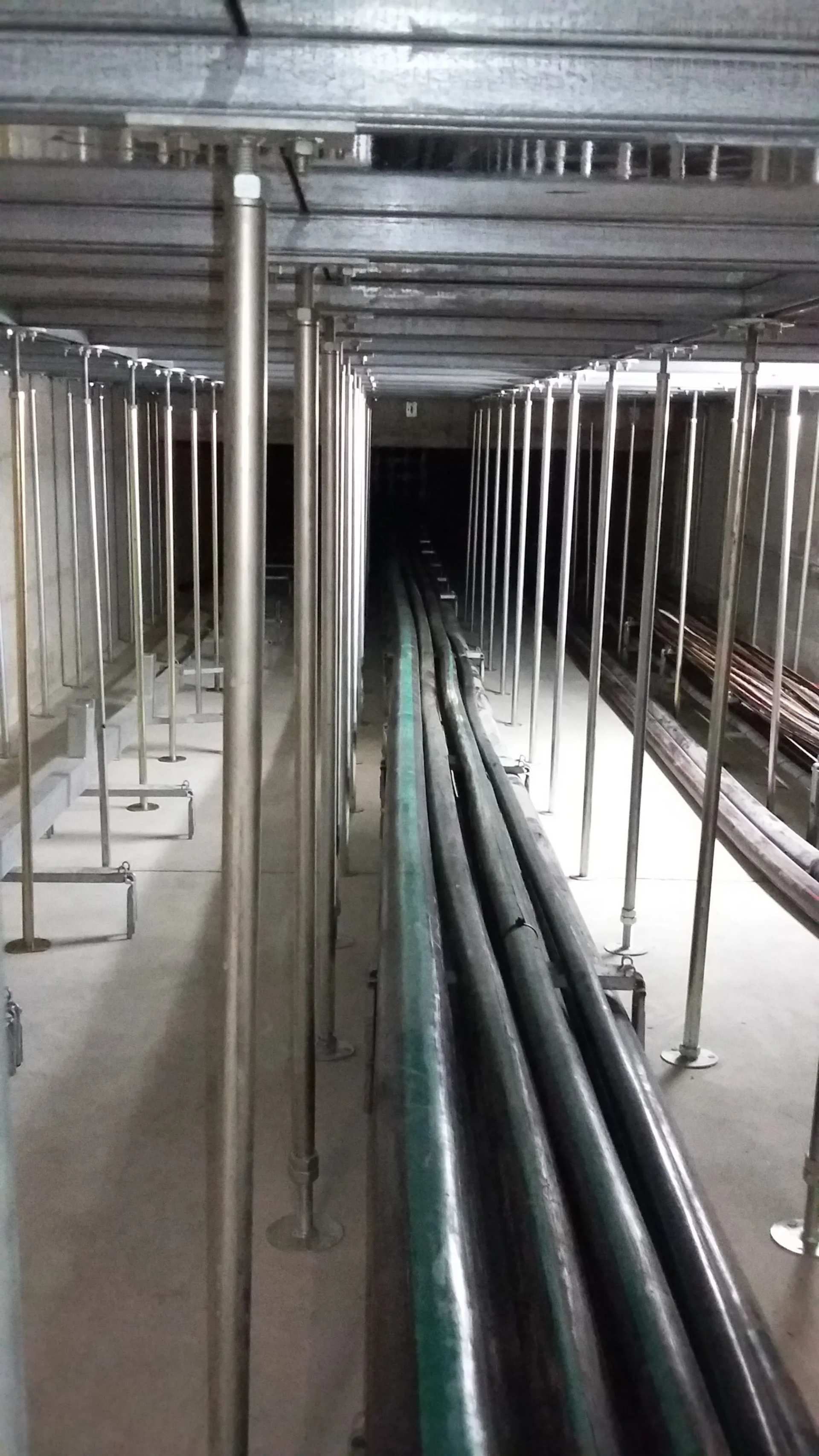 Des tuyaux et des supports métalliques longent un couloir sombre et étroit.