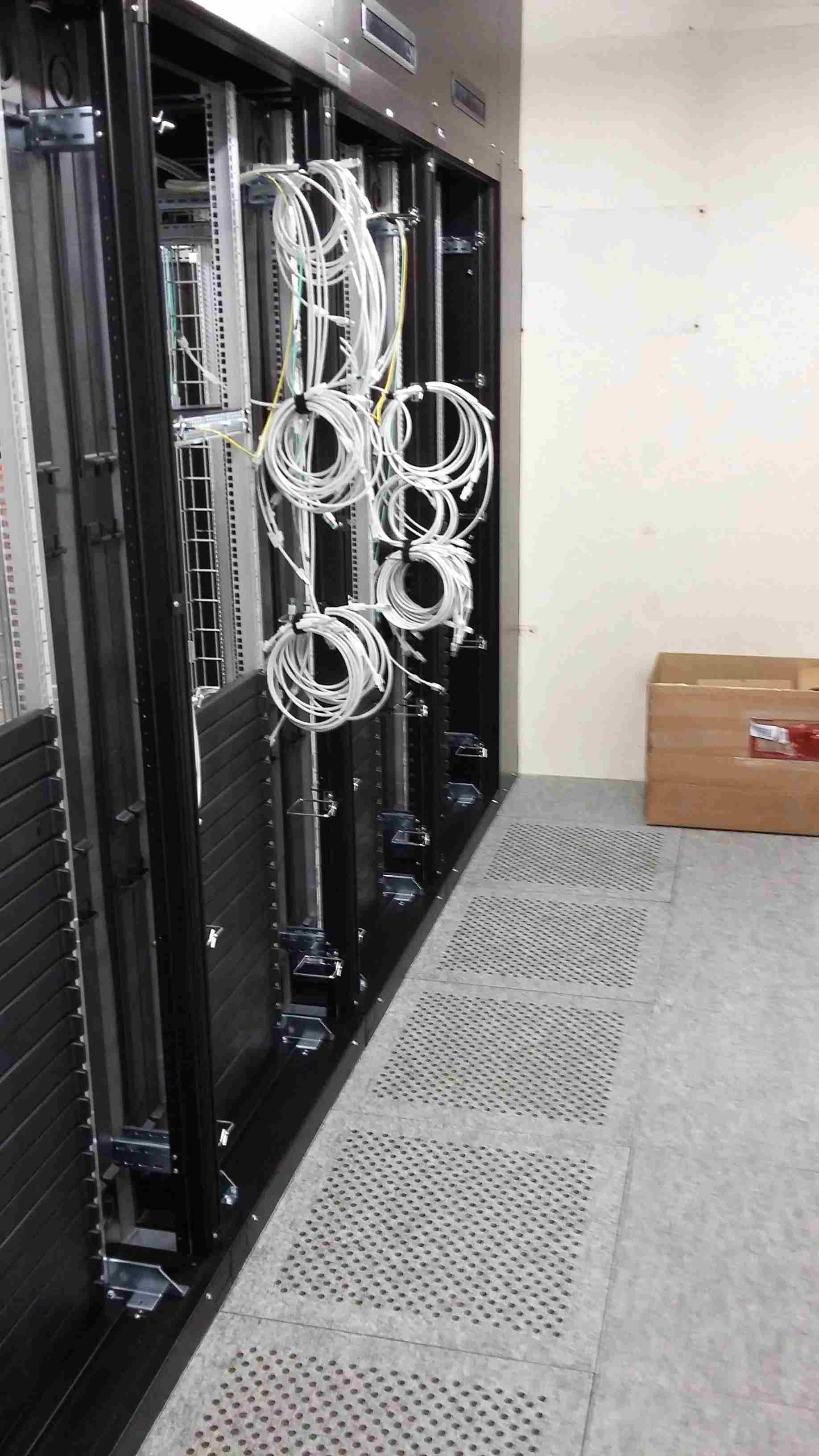 Baie de serveurs avec câbles blancs, placée dans une pièce au sol gris et avec un caisson en bois.
