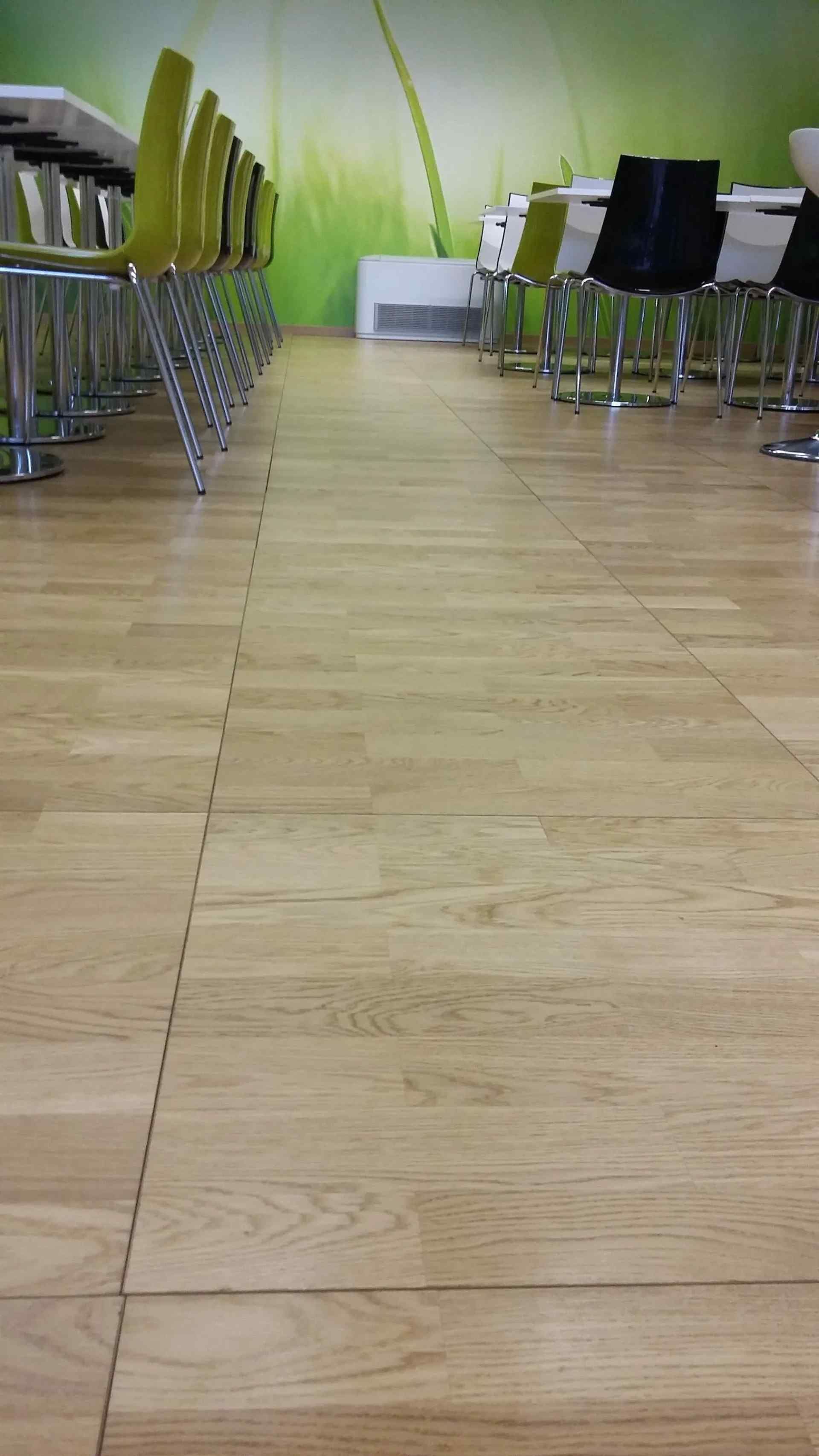 Sol en bois dans un café, avec des tables et des chaises vertes et noires le long des murs, et une fresque décorative au mur.