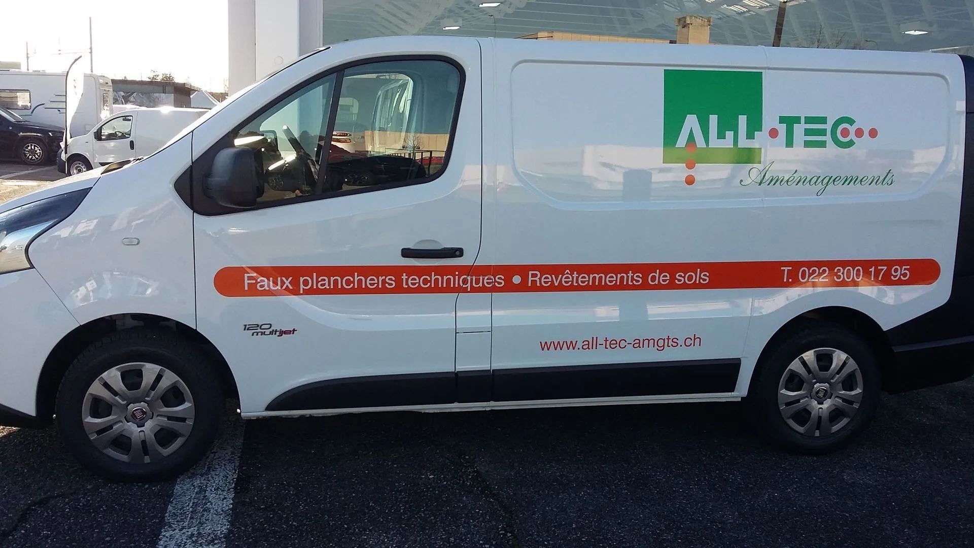 Fourgonnette blanche avec logo ALL-TEC, texte orange et numéro de téléphone, stationnée à l'extérieur.