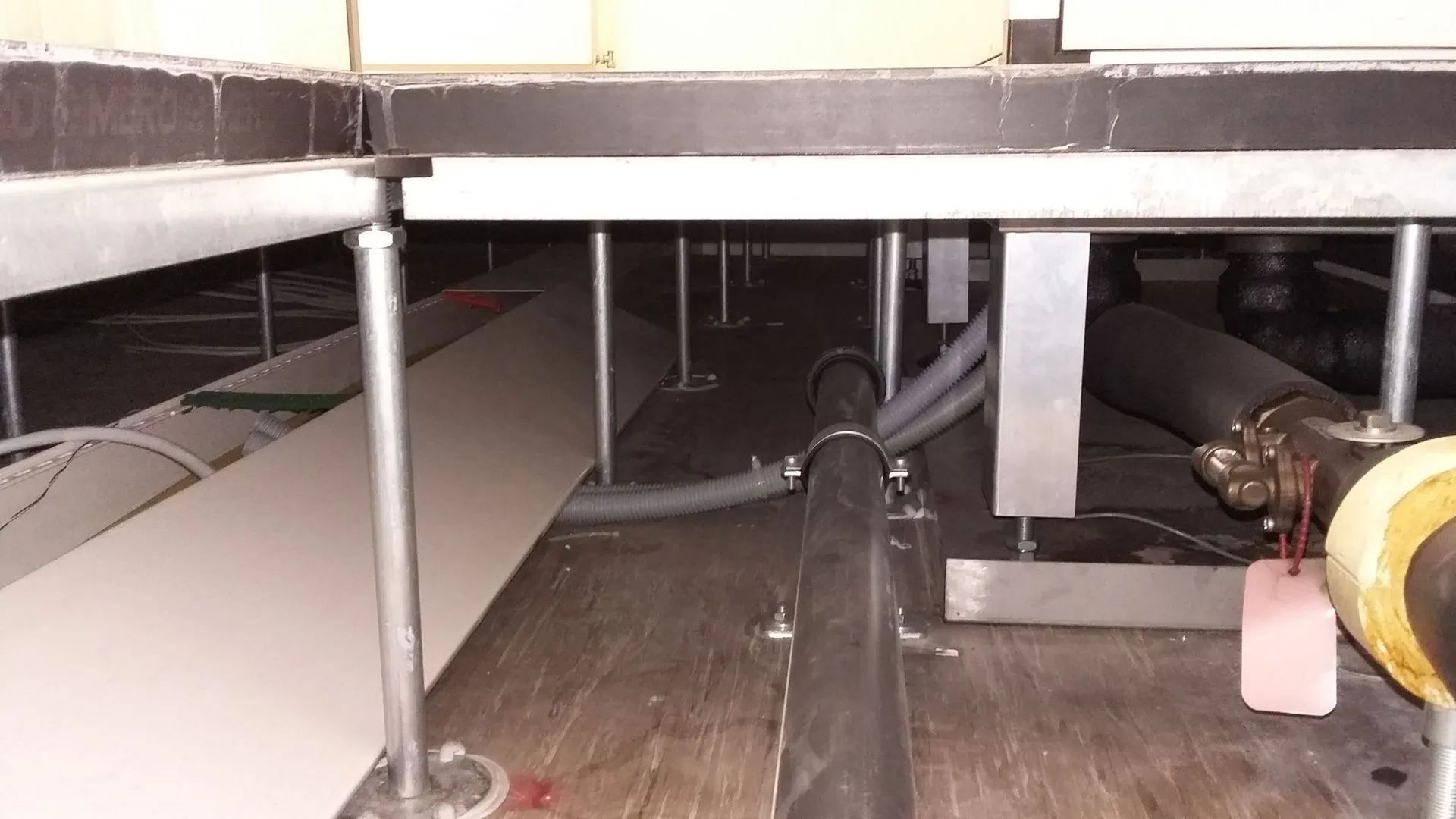 Face inférieure d'un plancher surélevé avec colonnes de support, tuyaux et câbles électriques.