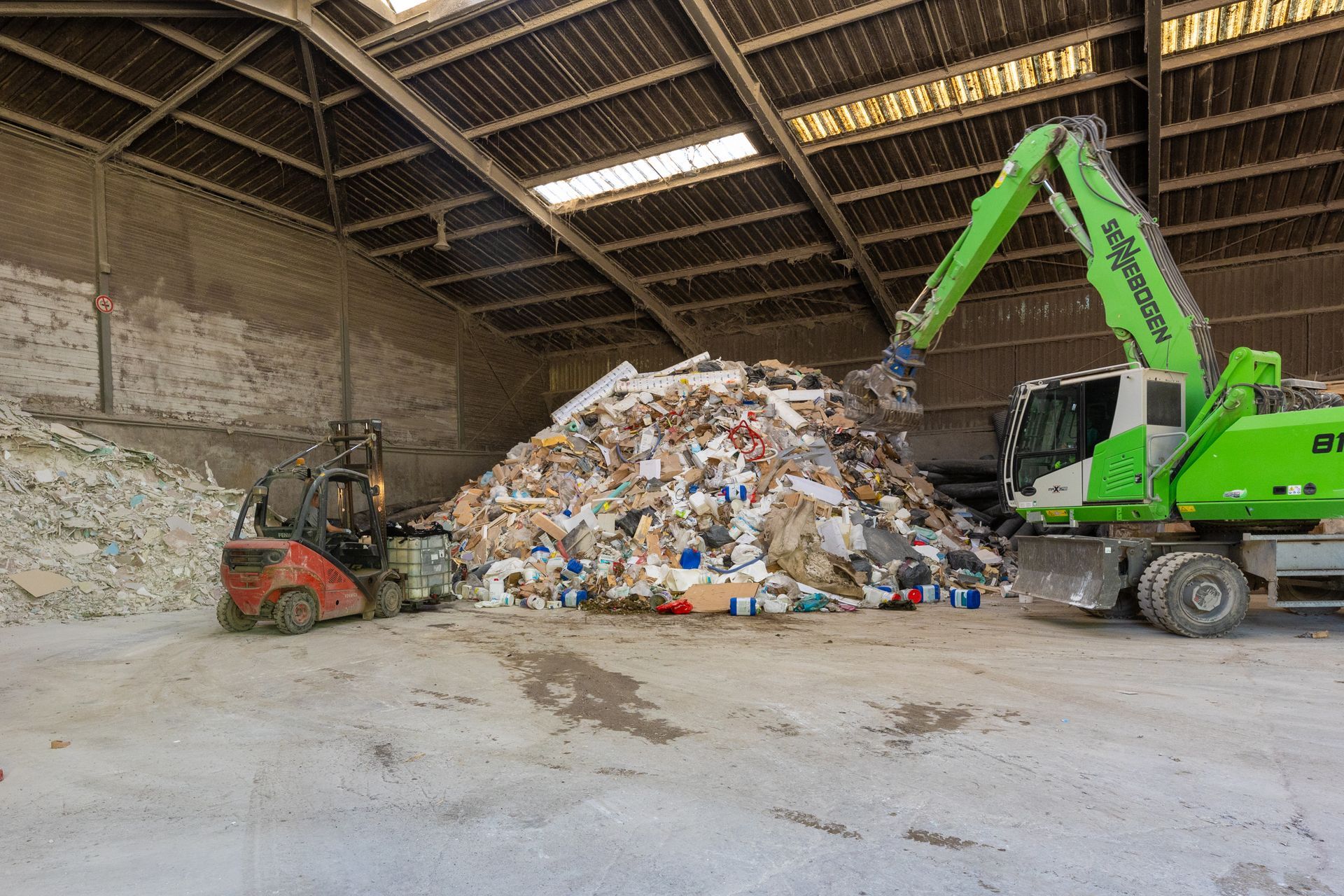Fenwick et grue à pince s'activant sur un tas de déchets dans un hangar.