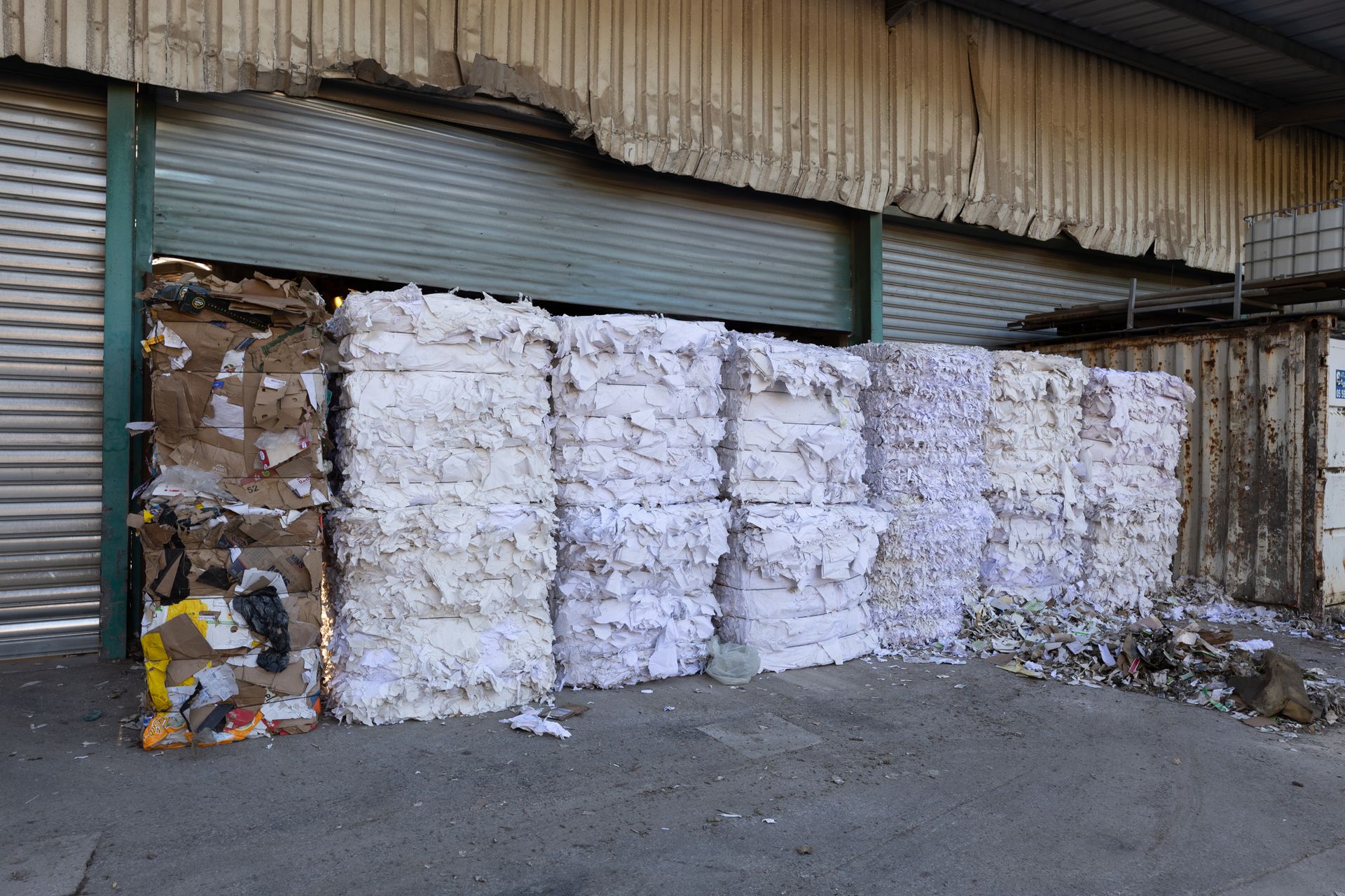 Des piles de papiers et cartons compactées à l'extérieur d'un hangar sur un site de déchetterie.