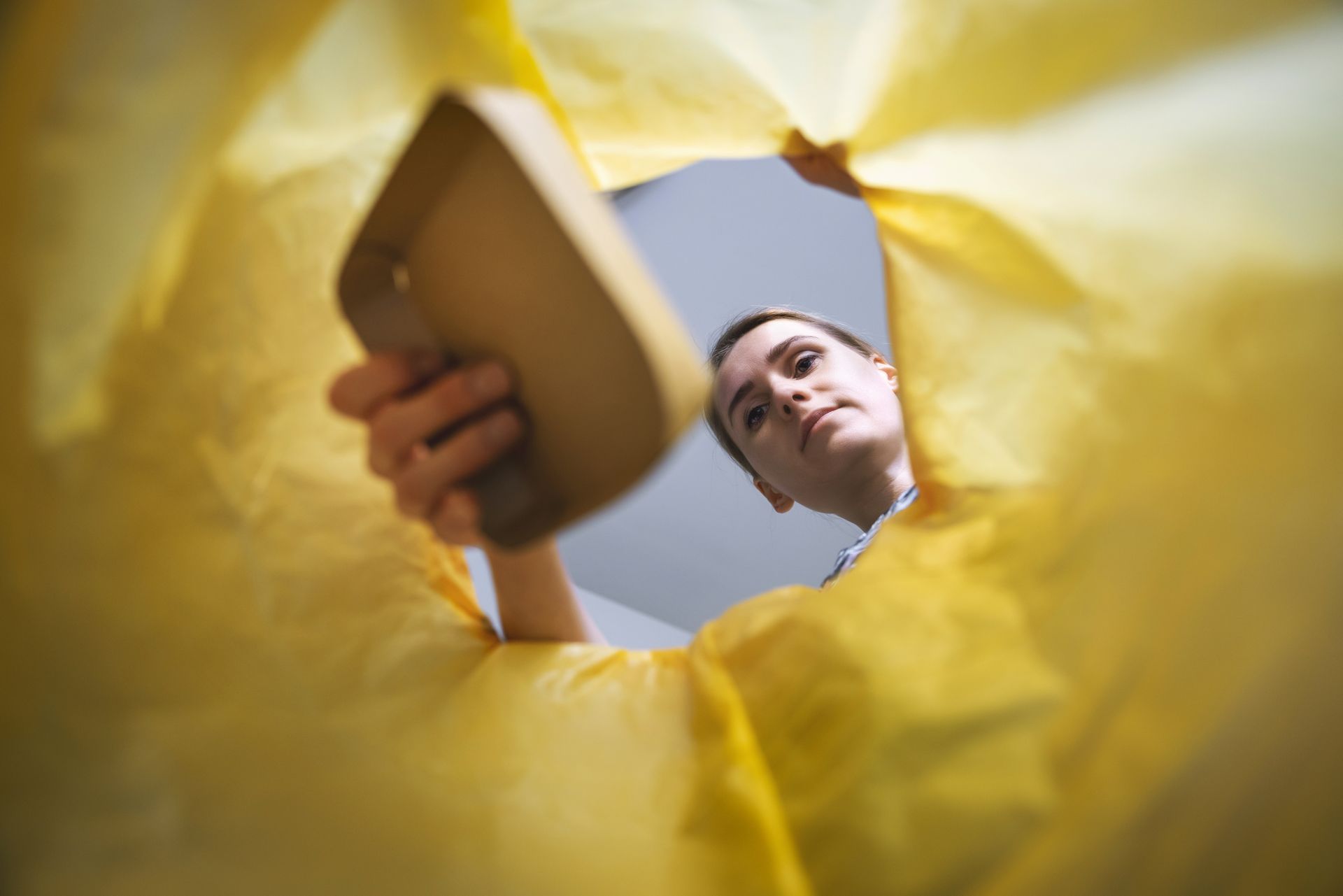 Vue en contre-plongée d'une femme déposant un déchet dans une poubelle de tri.