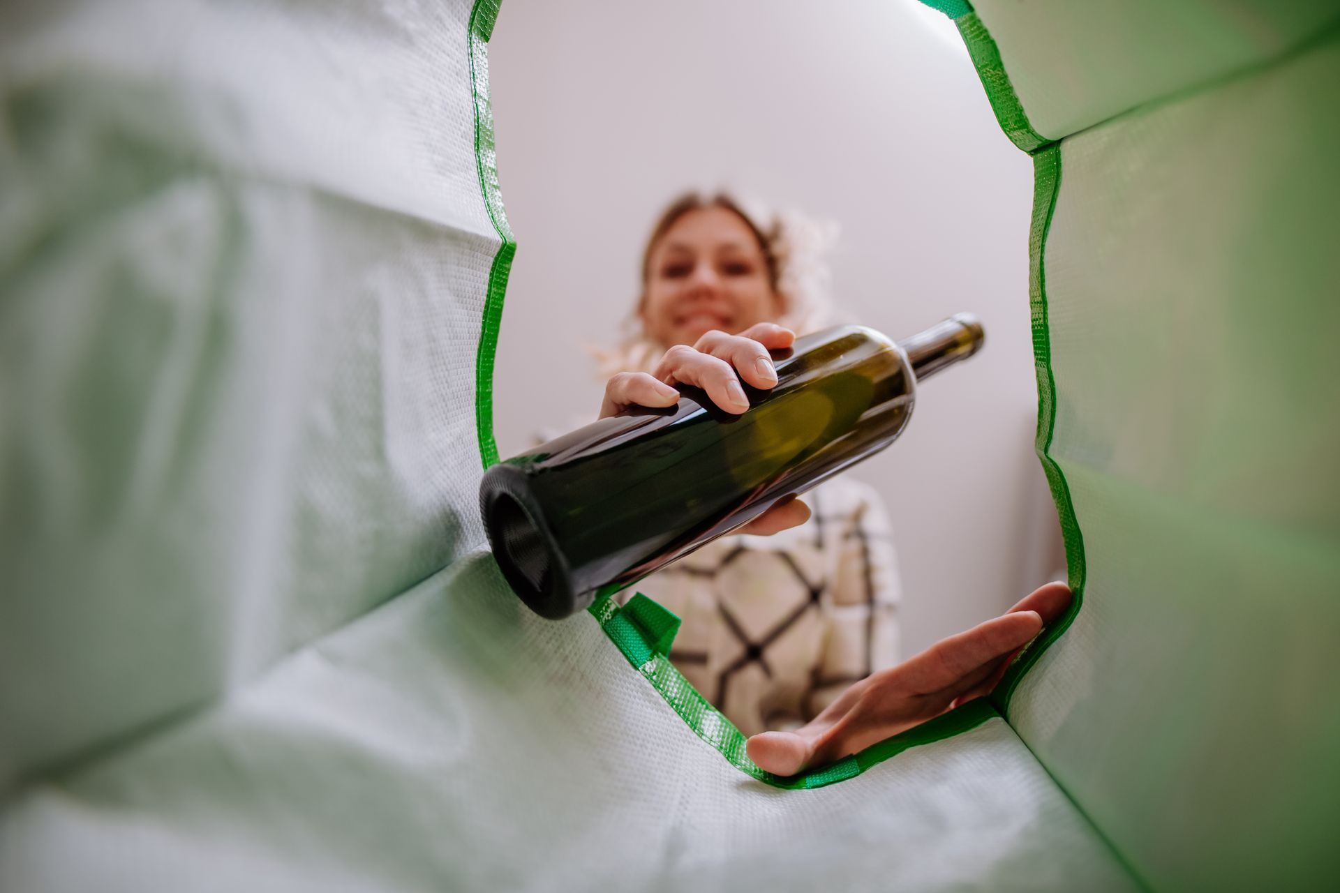 Vue en contre-plongée d'une femme déposant une bouteille en verre dans une poubelle de tri.