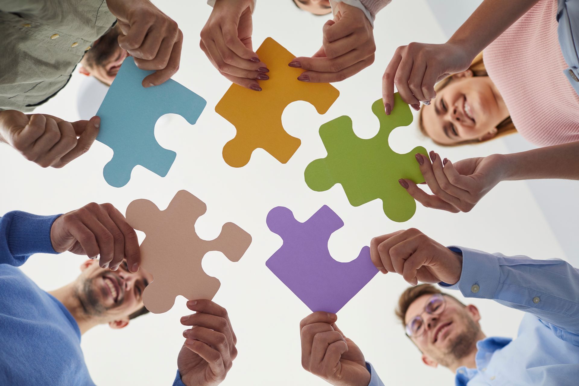 Vue en contre-plongée de personnes tenant des pièces de puzzle de différentes couleurs.